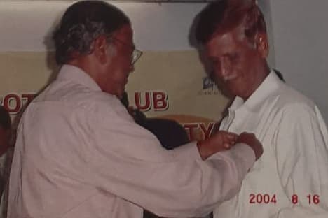 A Rotarian pinning the Rotary badge onto a new member's shirt at an induction, club banner behind them.